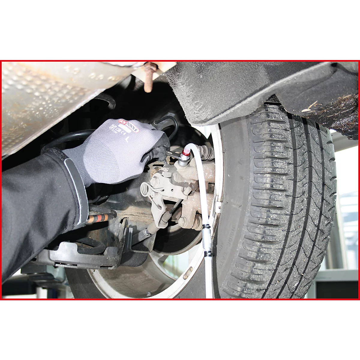 Nahaufnahme eines Mechanikers, der an einem Reifen arbeitet. Der Mann trägt Handschuhe. Das Bild zeigt einen Teil des Autos.